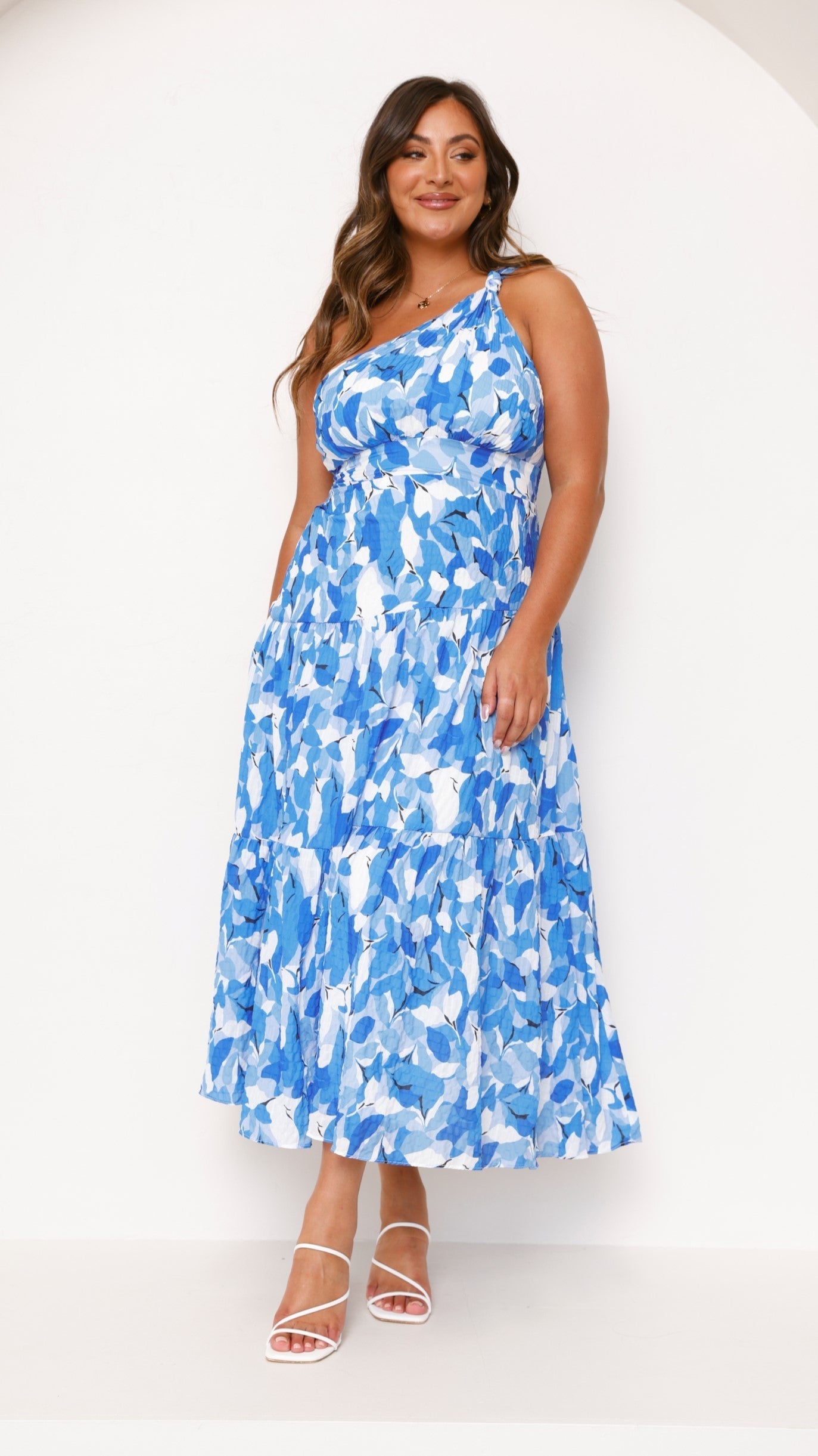 Women wearing the Elodie floral maxi dress by Harrow, a one-shoulder wedding guest dress with a dreamy floral pattern.